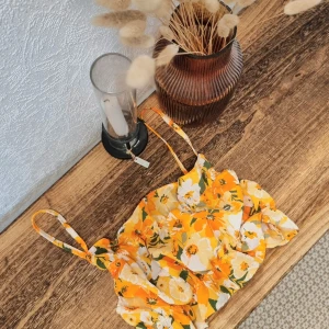 Gul blommig topp från Gina Tricot - Säljer en superfin blommig topp från H&M. Den har smala axelband och ett härligt blommönster i vitt och grönt. 