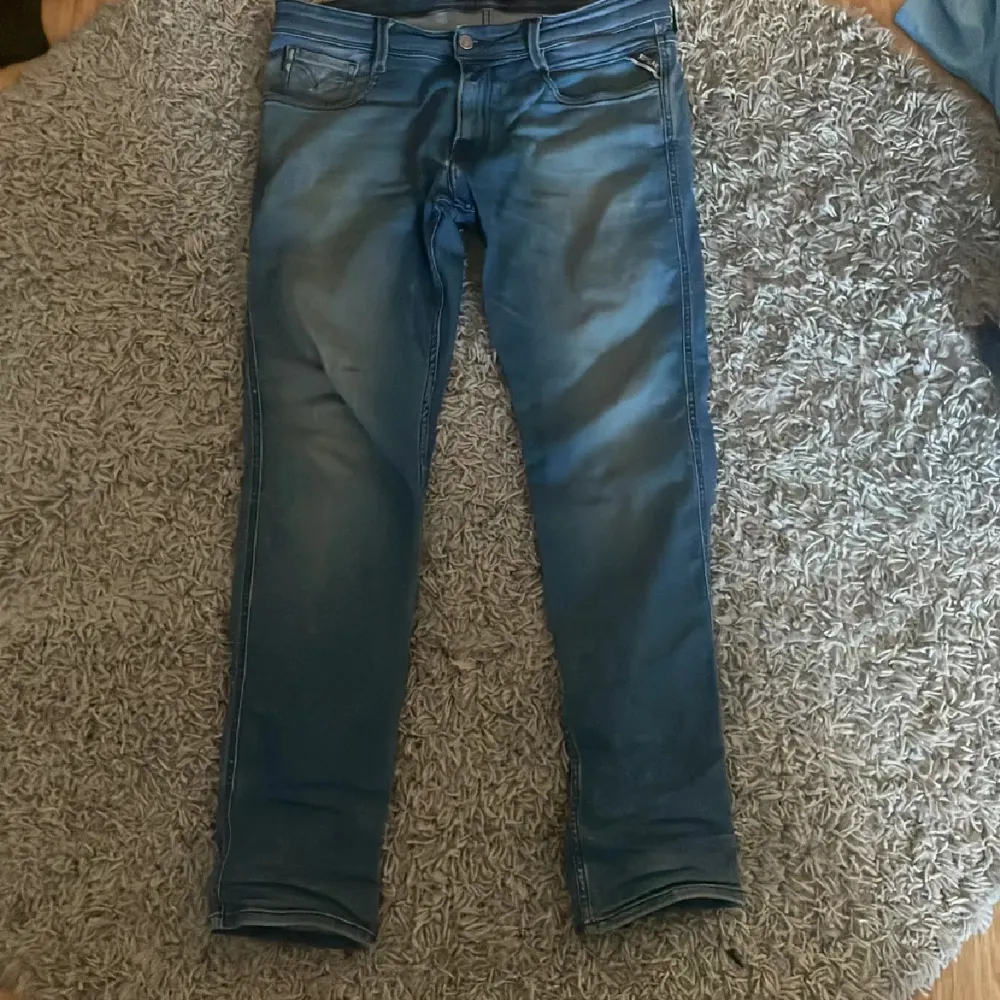 Säljer ett par snygga blå jeans från Replay, modell Anbass. De har en slim passform och är i nyskick. Perfekta för både vardag och fest! Jeansen har en klassisk femficksdesign och en bekväm midwaist. Materialet är mjukt och stretchigt, vilket gör dem superbekväma att ha på sig. Passa på att fynda dessa stilrena jeans!. Jeans & Byxor.