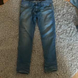 Säljer ett par snygga blå jeans från Replay, modell Anbass. De har en slim passform och är i nyskick. Perfekta för både vardag och fest! Jeansen har en klassisk femficksdesign och en bekväm midwaist. Materialet är mjukt och stretchigt, vilket gör dem superbekväma att ha på sig. Passa på att fynda dessa stilrena jeans!