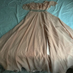 Champagnefärgad långklänning från Dressroom - Säljer en elegant champagnefärgad långklänning från Dressroom. Klänningen har vackra volanger upptill och ett glittrigt bälte i midjan med pärldetaljer. Perfekt för bal eller fest! 💫 används bara i 1 timme