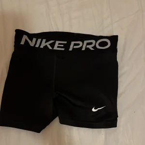 Svarta träningsshorts från Nike - Säljer ett par svarta Nike Pro träningsshorts. De är superbekväma och perfekta för gymmet eller löprundan. Shortsen har en tight passform och är gjorda i ett stretchigt material som andas. De har en bred resår i midjan med 'NIKE PRO' tryckt i grått.