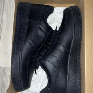 Svarta Nike Air Force sneakers - Säljer ett par klassiska svarta Nike Air Force sneakers i nyskick. De är helt svarta med snörning och har den ikoniska Air Force-sulan. Perfekta för både vardag och fest!