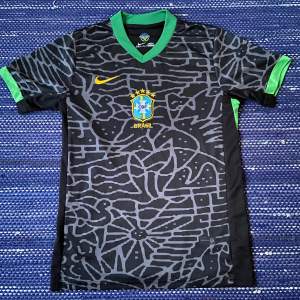 Säljer en snygg svart Brazil fotbollströja från Nike med gröna detaljer. Tröjan har ett coolt mönster och Brasilien-emblemet på bröstet. Den är kortärmad och perfekt för fotbollsfans!