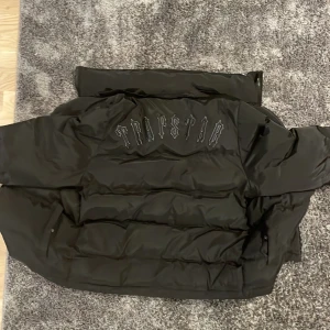 Svart trappsteg jacka - Svart trapstar jacka använd i kanske en månad, luvan på jackan ör trasig eftersom jag råkade dra sönder en av knapparna därför säljer jag inte den men luvan