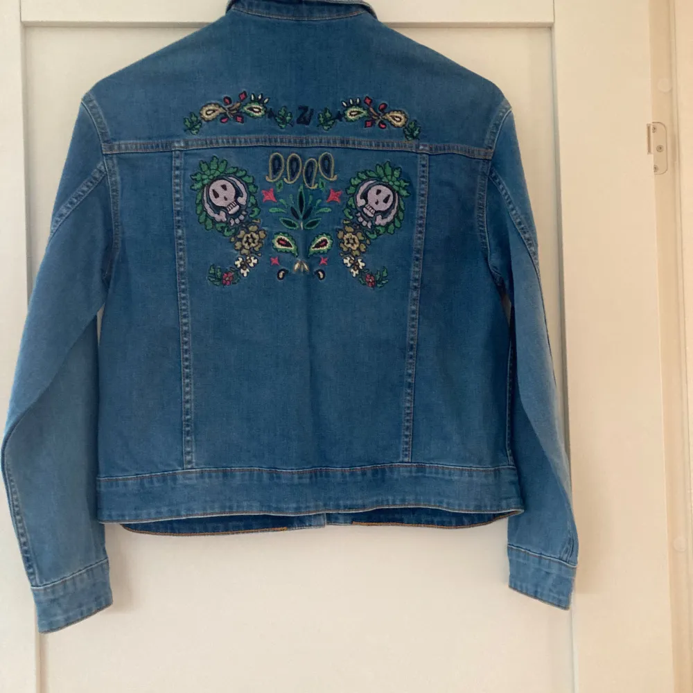 Säljer en snygg blå  jeansjacka från Zadig & Voltaire i nyskick. Jackan har coola broderier på ryggen med blommor och dödskallar. Den har långa ärmar och knappar framtill. Perfekt för vår och höst!. Jackor.