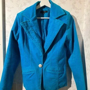 Blå kavaj med knapp - Snygg blå kavaj med en enkel knapp framtill. Perfekt för både vardag och fest. Den har en klassisk krage och långa ärmar. Passar bra till både jeans och kjol för en stilren look.