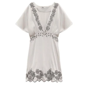 Silvrig klänning med broderade detaljer från Zara - Säljer en superfin silvrig klänning från Zara med vackra grå broderade blommor. Den har en v-ringad design och korta ärmar, perfekt för sommarens fester. Klänningen är i mycket bra skick och har en skön passform som är normal. Perfekt för en stilren och elegant look! Oanvänd med lappen kvar. Nypris: 1399kr