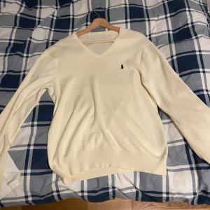 Ralph Lauren sweatshirt  - Säljer en stilren vit tröja från Ralph Lauren i mycket bra skick. Den har en klassisk v-ringning och är långärmad, perfekt för både höst och vår. Tröjan är i en mjuk och bekväm bomullsmix, vilket gör den både snygg och skön att bära. Den ikoniska loggan är broderad på bröstet. Passar perfekt till både jeans och chinos!