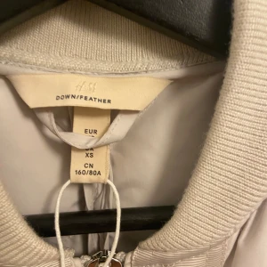 Beige quiltad dunjacka från H&M - Säljer en superfin beige quiltad dunjacka från H&M i storlek XS. Oversized. Jackan  har en dragkedja framtill och en praktisk bröstficka. Perfekt för kyliga höst- och vinterdagar. Den är i mycket bra skick och håller dig varm och stilren. Passar perfekt till både vardag och lite finare tillfällen.