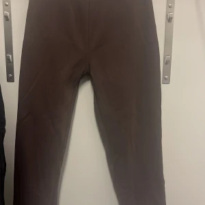 Bruna mjukisbyxor från Gina Tricot  - Säljer ett par bruna mjukisbyxor i bra skick från Gina Tricot. De är superbekväma och perfekta för en chill dag hemma eller en snabb tur till affären. Byxorna har en elastisk midja och muddar vid bensluten för extra komfort. Perfekta för höst och vinter!