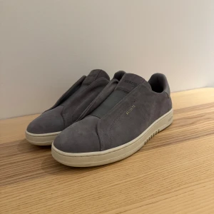 Axel Arigato Laceless gråa  - Säljer ett par stilrena grå sneakers från Axel Arigato i mycket bra skick. Skorna är i mocka med en vit sula och har en minimalistisk design. Perfekta för både vardag och fest. Storlek 44, skorna är aldrig använda då de var för stora. Köpte direkt i butik för nypris 2599kr. Orginalpåse och originallåda medföljer vid köp! Hör av dig vid instresse, kan gå ner i pris vid snabb och smidig affär. 