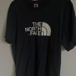 The North Face T-Shirt - Säljer en svart t-shirt från The North Face i bra skick. Den har en stor logga på framsidan och en mindre på baksidan. Perfekt för vardagsbruk eller träning. Skön och enkel stil som passar till det mesta. Hör av dig vid intresse!