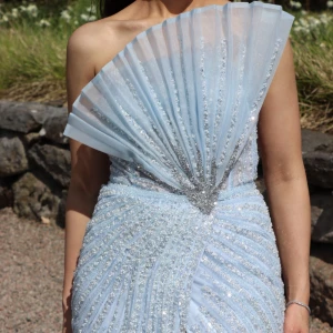 Ljusblå glittrig långklänning - Säljer en fantastisk ljusblå långklänning med glittriga detaljer och en elegant slits. Klänningen är från märket CATWALK, har en unik design med en veckad överdel som ger en extra touch av glamour. Perfekt för bal eller fest! Användes en kväll, storlek 36. Nypris 7000kr