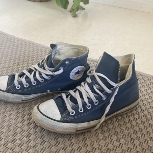 Blå Converse All Star sneakers - Säljer ett par klassiska blå Converse All Star sneakers i bra skick. De har en cool vintage-look med vita snören och den ikoniska loggan på sidan. Perfekta för vardagsbruk och ger en avslappnad stil. Passar både killar och tjejer!