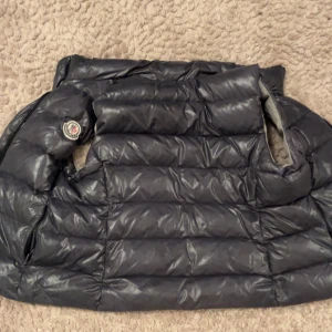 Svart väst från Moncler - Säljer en snygg svart dunjacka från Moncler i mycket bra skick. Jackan är perfekt för kalla dagar med sitt varma dunfoder. Den har en klassisk design med Moncler-logga på ärmen. Passar perfekt för både vardag och festliga tillfällen.