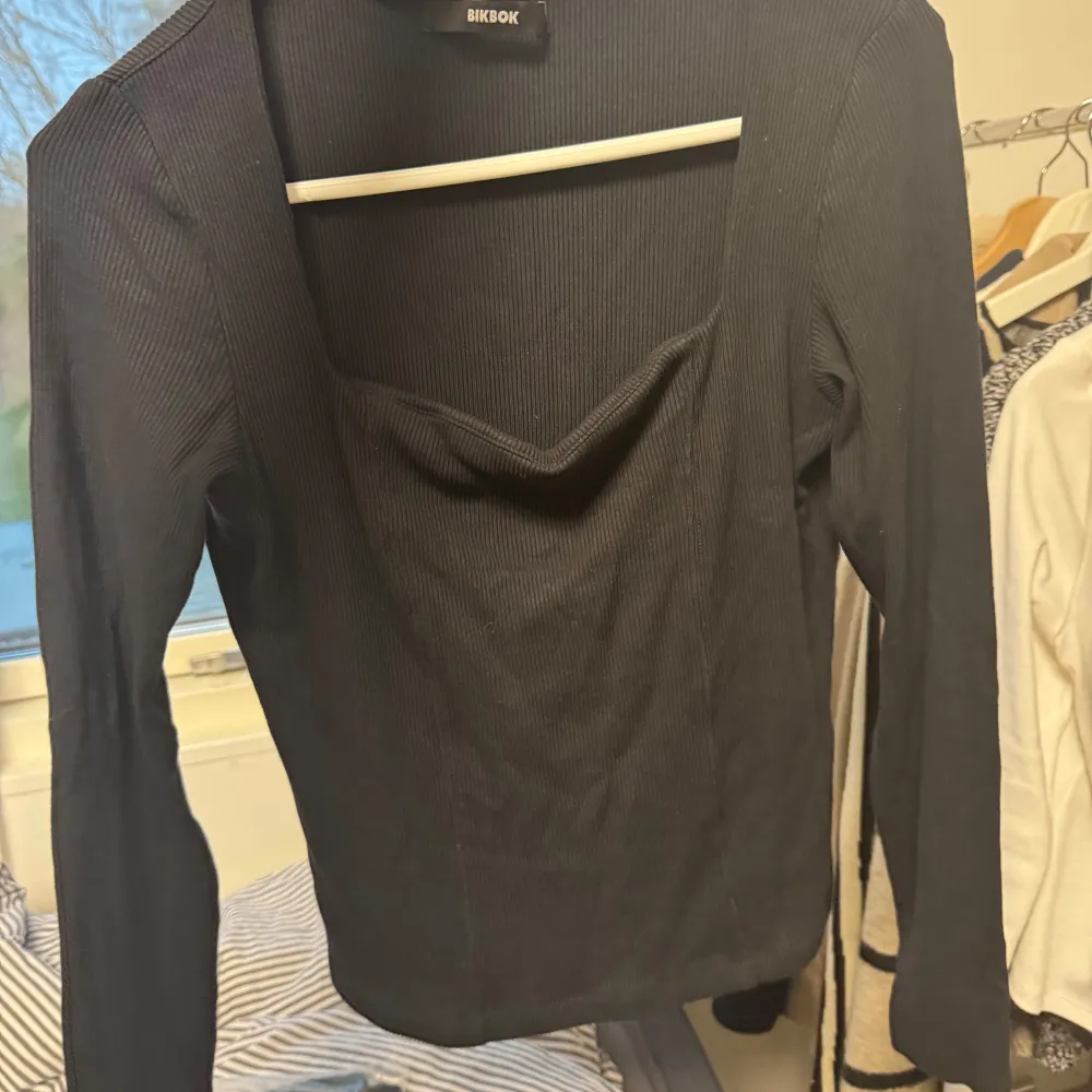 Säljer en snygg svart ribbad topp från BikBok i storlek M. Toppen har en stilren design med långa ärmar och en smickrande v-ringad hals. Perfekt för både vardag och fest! 🖤Lite fläckar som visar att den är använd men inget man märker då den är mörk. Neuletakit & Villapaidat.