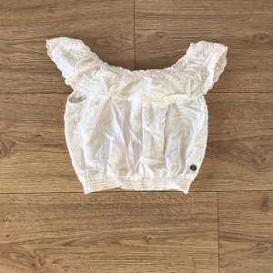 Vit offshoulder topp med spetsdetaljer - Säljer en söt vit offshoulder topp med vackra spetsdetaljer. Toppen har en elastisk kant vid midjan och är perfekt för sommardagar. Den är i bra skick och passar både till vardags och festliga tillfällen. Perfekt för att känna sig extra fin! 🌸