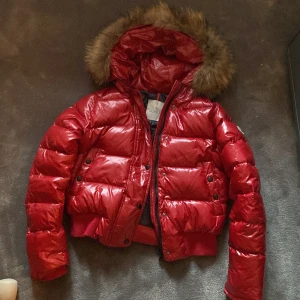 Röd dunjacka från Moncler - Säljer en snygg vinröd pepper grenoble dunjacka från Moncler med pälskantad huva. Jackan har en glansig finish och stängs med dragkedja och knappar. Den är i nyskick förutom minimal slitning på knapparna. Perfekt nu för vintern.                  Storlek 34/XS