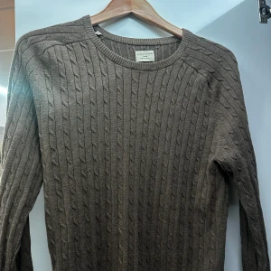Brun stickad tröja från Selected Homme - Säljer en snygg brun stickad tröja från Selected Homme. Perfekt för höst och vinter med sitt klassiska kabelstickade mönster. Tröjan har en rund hals och långa ärmar, vilket gör den både stilren och bekväm. Passar perfekt till både vardag och lite finare tillfällen. Något mindre i storlek.