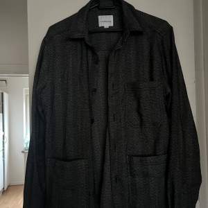 Säljer en snygg grå overshirt från Lindbergh i storlek S. Den har ett diskret mönster och är perfekt för höst och vår. Skjortan har långa ärmar och knappar framtill. Passar både till vardags och lite mer uppklädda tillfällen.