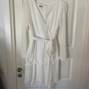 Vit omlottklänning från Dennis Maglic - Säljer en vit omlottklänning från Dennis Maglic i storlek M. Klänningen har långa ärmar och ett knytband i midjan. Den är lite glittrig också. Perfekt till studenten eller liknande 