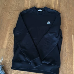Svart tröja från Moncler - Säljer en stilren svart tröja från Moncler i mycket bra skick. Den har en klassisk rund hals och Monclers logga broderad på bröstet. Perfekt för både vardag och fest. Passar till allt och är superbekväm! Pris går absolut att diskuteras🤝köpt för 5000 på Monclers hemsida.