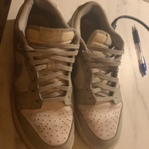 Nike Dunk i beige och vit - Säljer ett par Nike Dunk sneakers i beige och vit. Perfekta och sköna att gå i på sommaren och vintern. Funkar bra till både byxor och shorts! Som ni ser lite på bilderna så har de rätt mycket starloss. Men skorna är väldigt enkla att tvätta. Annars är det väldigt bra skick! Vid frågor eller funderingar hör av er! 