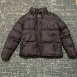 Svart pufferjacka från Neomondo - Säljer en svart pufferjacka från Neomondo i storlek M. Jackan är perfekt för kalla dagar med sin tjocka vaddering och dragkedja framtill. Den har en stilren design och är superbekväm att ha på sig. Passar både till vardags och utomhus aktiviteter. Original Pris:1100kr