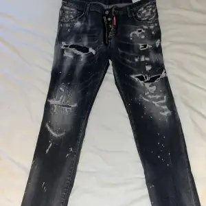 Säljer ett par svarta jeans från dsquared2 med coola slitningar och färgstänk. De har en normal passform . Jeansen har knappar och dragkedja framtill samt fickor. Byxorna är äkta! 