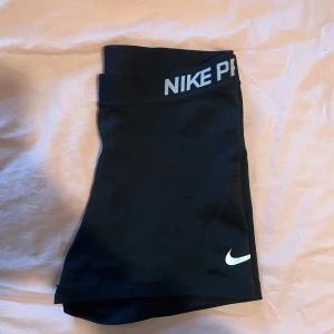 Svarta träningsshorts från Nike pro - Säljer ett par svarta träningsshorts från Nike Pro med Dri-FIT-teknologi. De är tighta och perfekta för träning. Shortsen har en elastisk midja med Nike-logga och är i mycket bra skick. Perfekta för gymmet eller löprundan! 