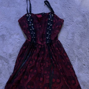 Svart och röd klänning med snörning - Säljer en cool svart och röd klänning med snörning framtill. Klänningen har ett unikt mönster och är perfekt för festliga tillfällen. Den är axelbandslös och har en snygg passform som framhäver figuren. 