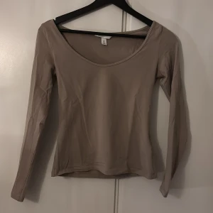 Beige långärmad topp från H&M - Säljer en stilren beige långärmad topp från H&M i storlek S. Perfekt för både vardag och festliga tillfällen. Toppen har en enkel design med rund halsringning och är i mycket bra skick. Passar perfekt till jeans eller kjol för en avslappnad look.