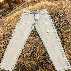 Ljusa jeans med slitningar - Säljer ett par ljusa jeans i storlek 32 med coola slitningar på framsidan. De har en klassisk femficksdesign och är perfekta för en avslappnad stil. Passar bra till både vardag och fest. Sköna och trendiga, ett måste i garderoben!