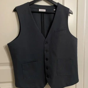 Väst mörkgrå stl L från Lindberg - Mörkgrå väst från Lindbergh. Västen är detaljerad med fickor vilket gör den lyxig. Västen har stl L och är aldrig använd.