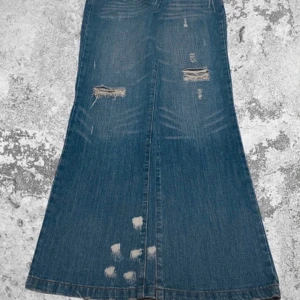 Blå bootcut jeans med slitningar - Säljer ett par snygga blå bootcut jeans med coola slitningar och broderade bakfickor. Perfekta för en avslappnad stil med lite edge. De har en klassisk femficksdesign och är i bra skick. Passar perfekt till både vardag och fest!     Midja: 87cm.     Total längd: 107cm