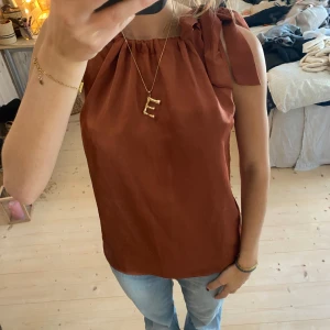 Brun ärmlös topp med knytband - Säljer en snygg brun ärmlös topp med knytband vid axlarna. Perfekt för sommardagar eller en avslappnad kväll. Toppen har en lös passform och är gjord i ett mjukt material som känns skönt mot huden. Passar bra till jeans eller kjol för en chic look❤️❤️❤️