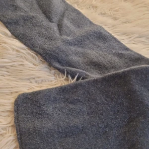 Grå kort halsduk i ull - Säljer ett par grå byxor i ullmaterial. Perfekta för kyligare dagar med sin mjuka och varma känsla. Byxorna har en rak passform och är i mycket bra skick. Perfekta för både vardag och mer uppklädda tillfällen.