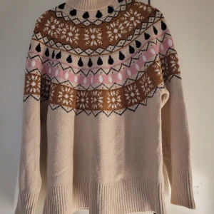 Beige stickad tröja från Gina Tricot - Superfin beige stickad tröja från Gina Tricot i storlek S. Den har ett snyggt mönster i brunt, rosa och svart runt halsen. Perfekt för kyliga dagar med sina långa ärmar och ribbade muddar. Passar både till vardags och mysiga vinterkvällar. 🧡