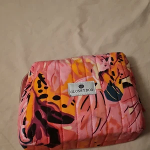 Färgglad necessär från Glossybox - Säljer en superfin och färgglad necessär från Glossybox. Den har ett quiltat mönster i rosa, orange och svart med en praktisk dragkedja. Perfekt för att förvara smink eller andra småsaker. Den är i mycket bra skick och redo för nya äventyr!