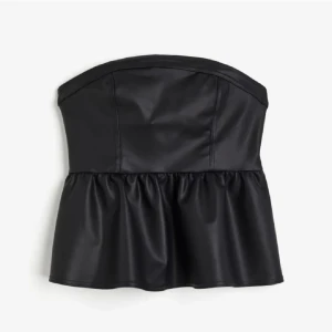 Svart axelbandslös topp - Snygg svart axelbandslös topp i skinnimitation med en volangdetalj nedtill. Perfekt för en utekväll eller fest! Toppen har en tight passform upptill och en lösare volang som ger en fin siluett.