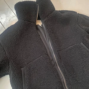 Svart HM Teddy jacka  - Mysig svart teddyjacka i mycket bra skick. Perfekt för höst och vinter med sin varma och fluffiga design. Jackan har en dragkedja framtill och långa ärmar.