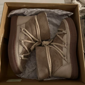 Beige boots från Inuikii - Säljer ett par snygga och varma beige boots från Inuikii. De är i mycket bra skick och har en cool snörning framtill. Perfekta för vintern med sin robusta sula och mjuka insida. De är gjorda i skinn och mocka vilket ger en lyxig känsla. Storlek 36. Nypris: 2999
