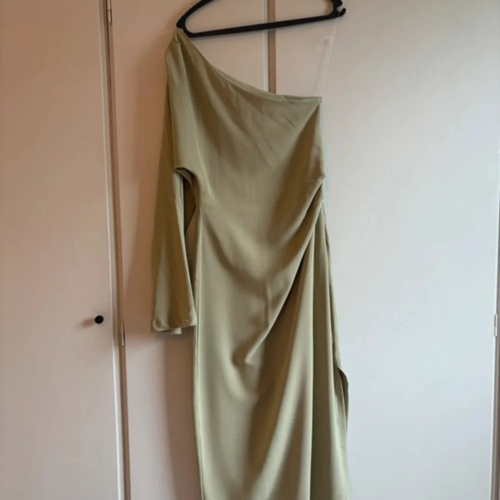 Snygg beige/grön oneshoulder långklänning i ett mjukt och bekvämt material som faller fint. Perfekt för en elegant kväll eller fest. Klänningen har en stilren design med en lång ärm och en smickrande passform. Ett måste för garderoben!. Klänningar.