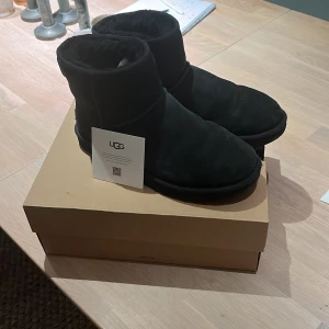 Svarta vinterskor från UGG - Säljer ett par svarta UGG skor i väldigt fint skick. De är gjorda av mocka och har en mysig, varm insida perfekt för vintern. Skorna kommer i originalförpackning och är helt oanvända. Perfekta för att hålla fötterna varma och stiliga under kalla dagar! Mitt pris 999 Kr