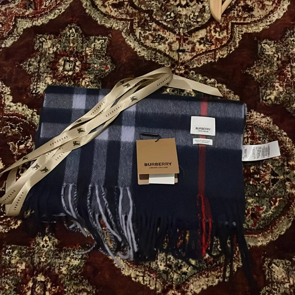 Säljer en superfin rutig halsduk från Burberry i 100% kashmir. Den har en klassisk design med rutor i svart, grått och rött. Perfekt för att hålla sig varm och stilren under kyliga dagar. Halsduken är i nytt skick och kommer med originalförpackning. Hör av dig vid frågor!. Övrigt.