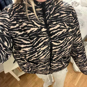 Zebramönstrad pufferjacka - Säljer en supercool zebramönstrad pufferjacka från H&M i svart och beige. Jackan har en dragkedja framtill och är perfekt för höst och vinter. Den är även lite croppad. 