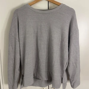 Grå stickad tröja från Holly's - Säljer en supermysig grå stickad tröja från Holly's i storlek M. Den har långa ärmar och ribbade detaljer vid hals, ärmslut och nederkant. Perfekt för kyliga dagar och passar till allt! 🩶