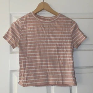 Randig t-shirt från H&M Divided - Säljer en superfin randig crop-top från H&M Divided i storlek L. Den är i en mjuk rosa färg med vita ränder och har en klassisk rund hals. Perfekt för en avslappnad stil och passar till både jeans och kjol. Använd ett par gånger men i bra skick!