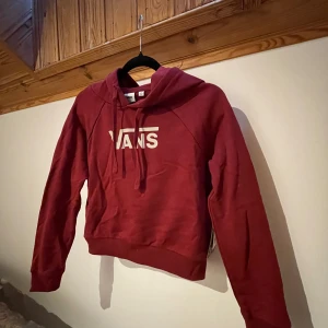 Vinröd hoodie från Vans - Säljer en snygg vinröd hoodie från Vans med logga på bröstet. Tröjan är croppad. Aldrig använd.