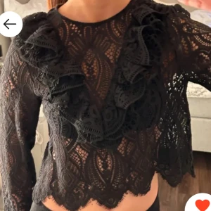 Svart spetsblus från Zara - Snygg svart spetsblus från Zara med volangdetaljer framtill. Blusen har långärmade ärmar och ett vackert mönster som ger en elegant look. Perfekt för att lyfta vilken outfit som helst.